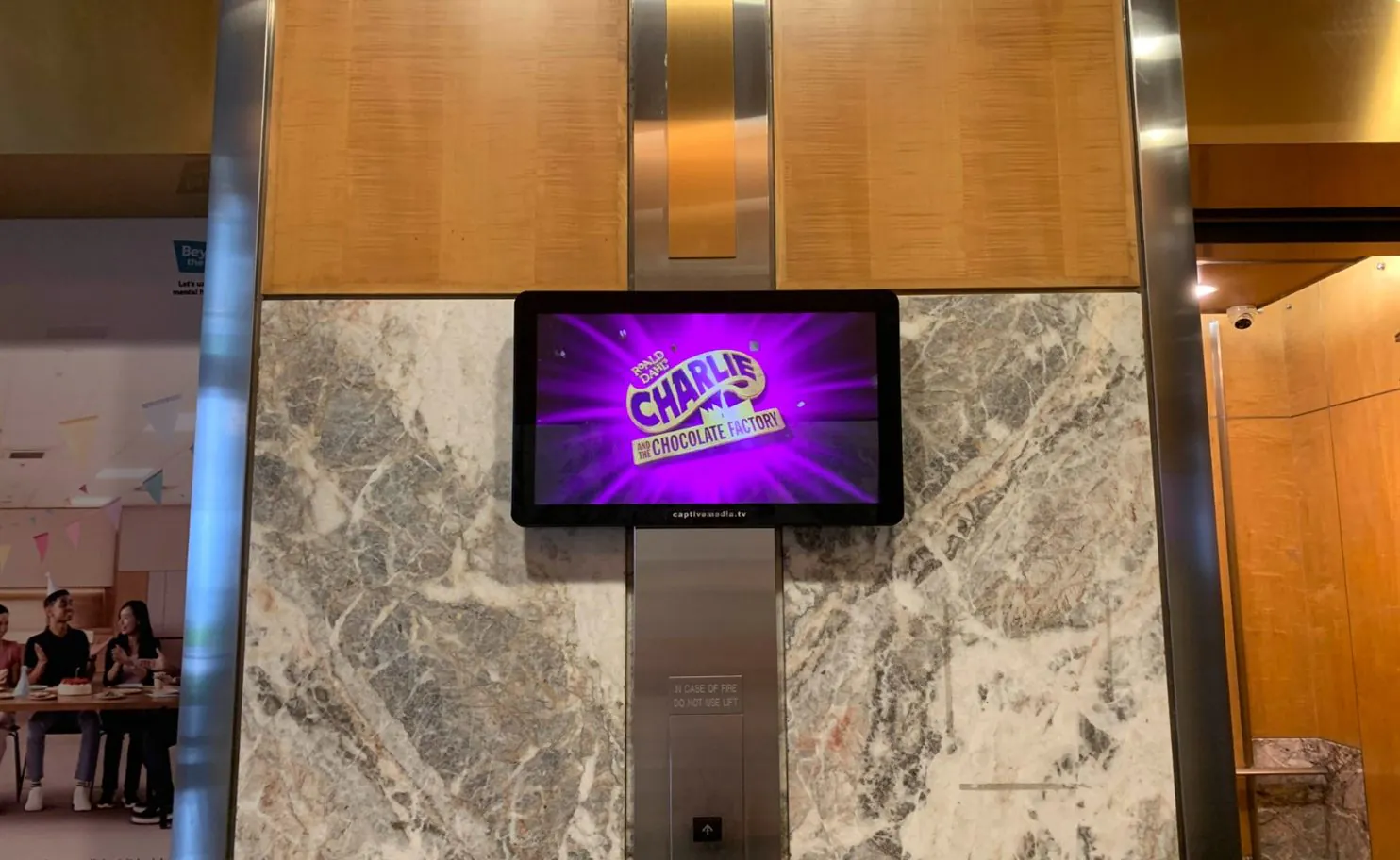 Digital screen showing a Charlie and the Chocolate Factory advertisement in an office building lift lobby