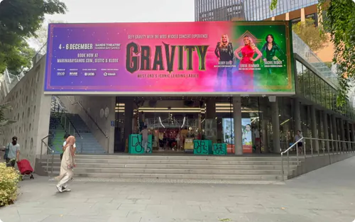 Digital billboard above the Design Orchard entrance on Orchard Road, Singapore, showing a GRAVITY concert ad